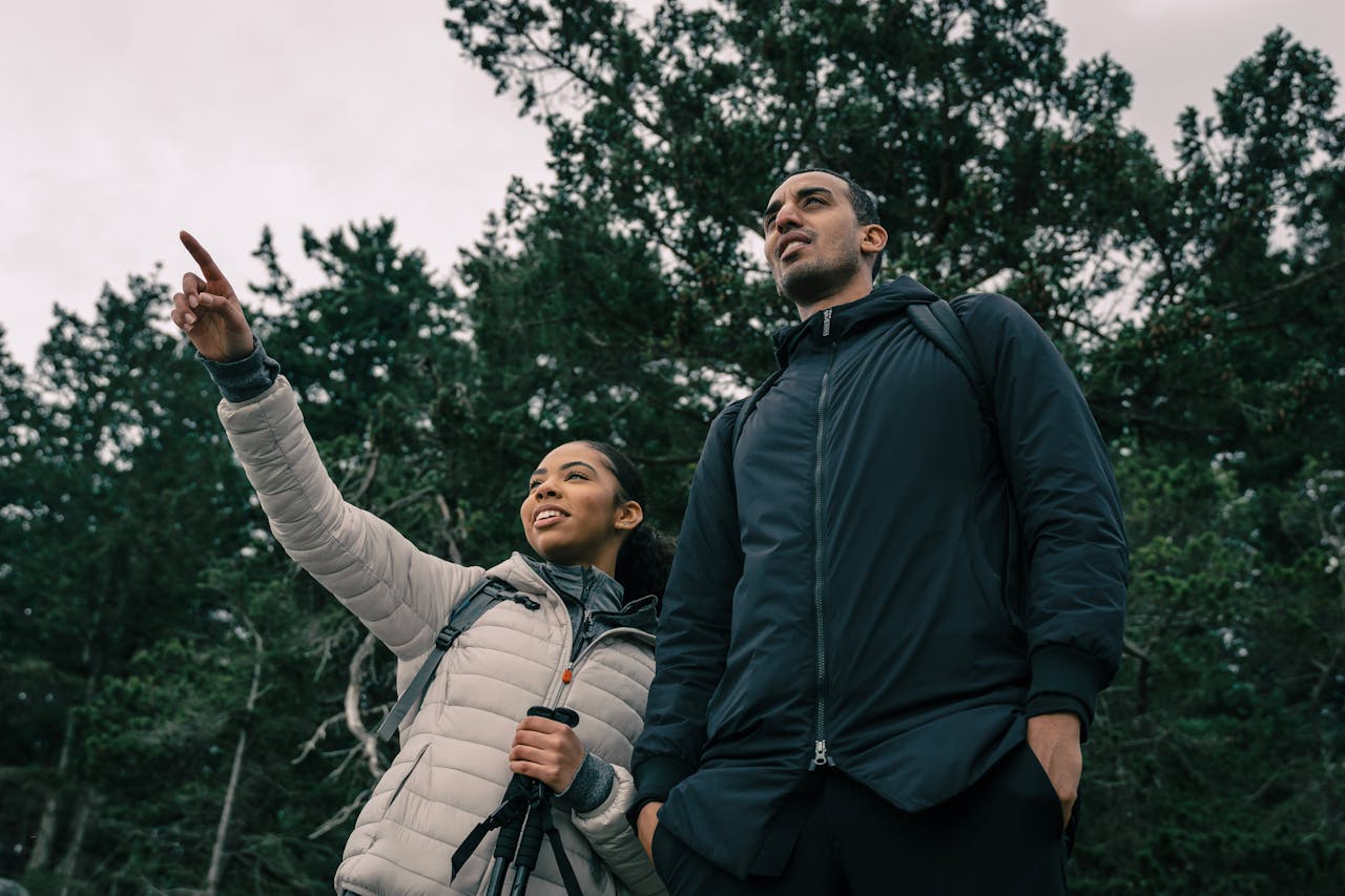 a young black man and woman facing the camera in hiking gear looking out at a view with the woman pointing