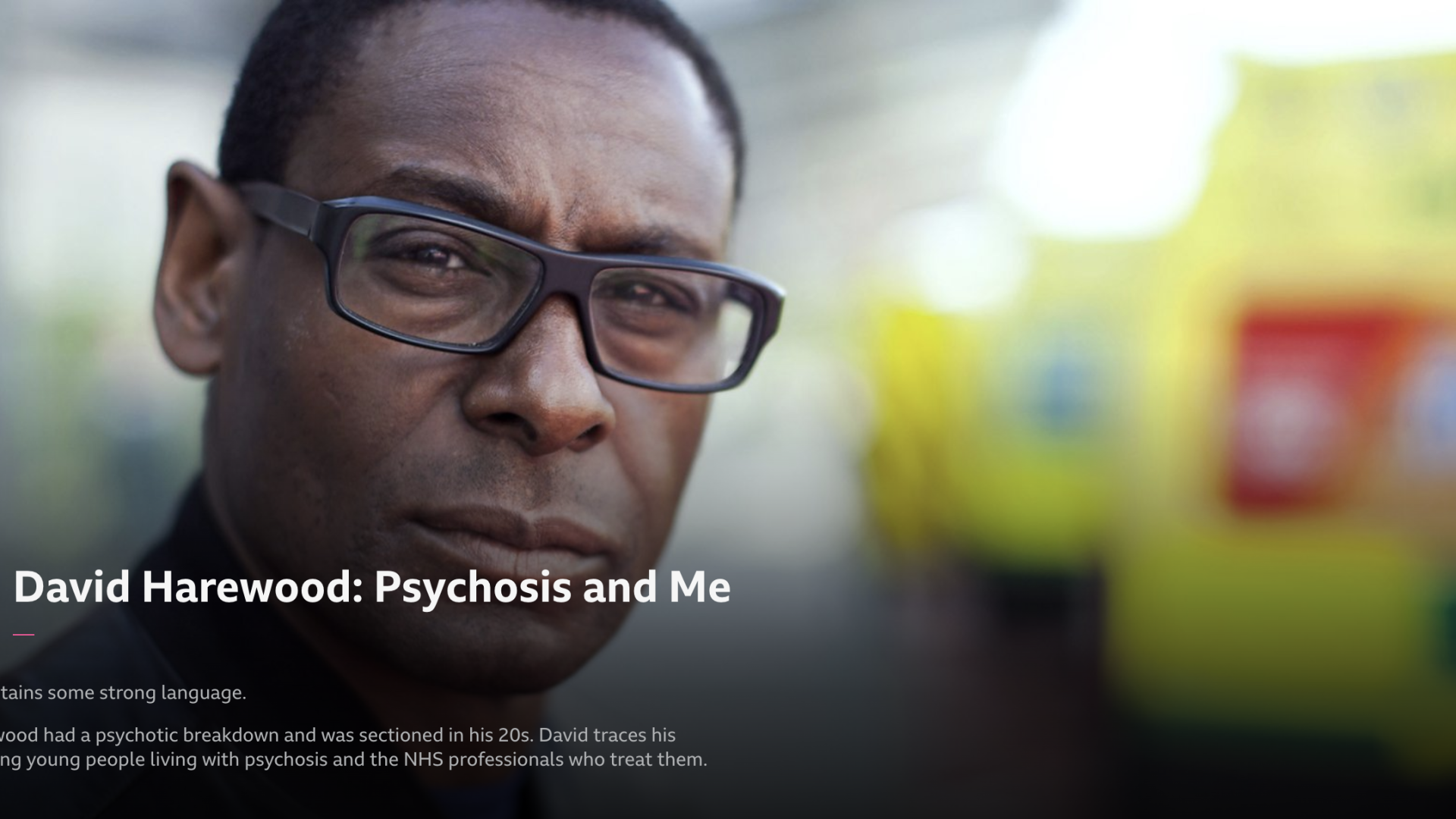 A screenshot of the documentary featuring David Harewood. He is black with short black hair and thick black rimmed glasses and he is close to the camera and looking at the viewer.