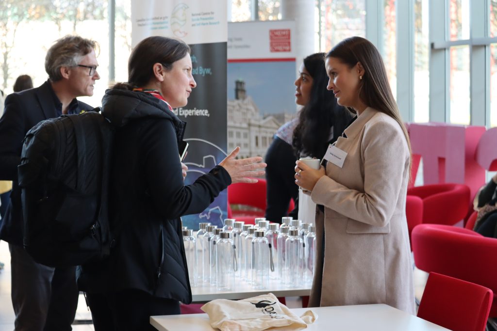 Two white women with dark hair speaking at the Hub event. THe lady on the left is in dark clothing with long brown hair in a ponytail. And the woman on the right has long brown hair which she wears down and a light jacket. 